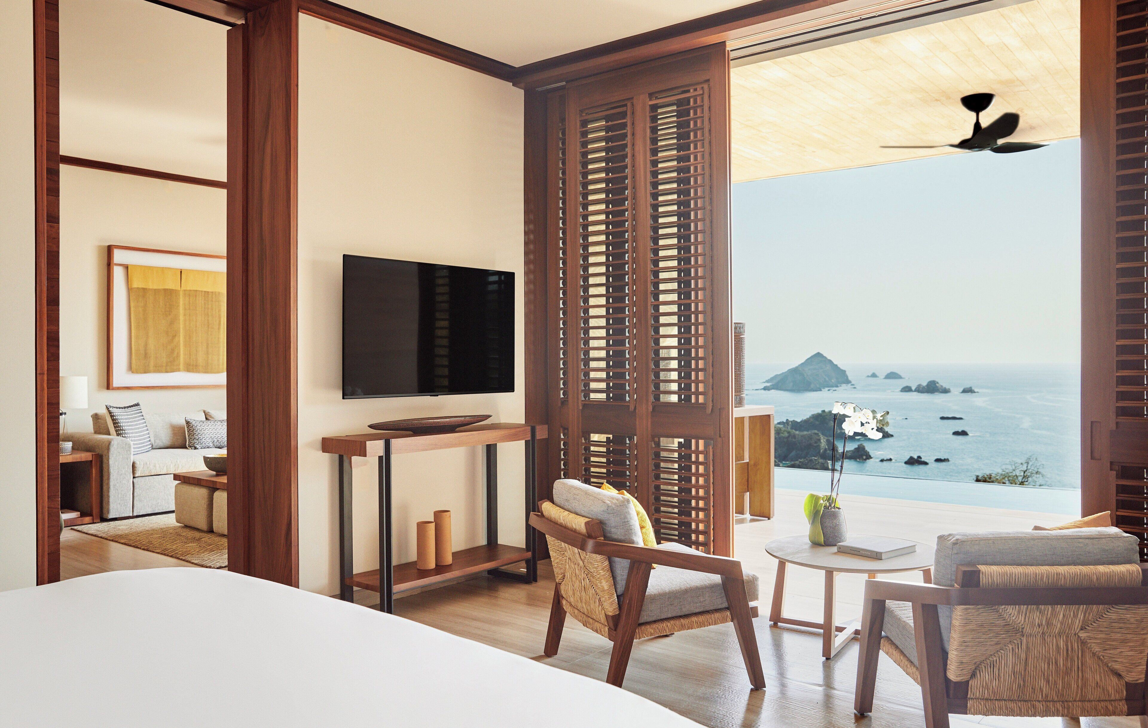 A modern hotel room with a large bed, a TV, a wooden partition, and a view of the ocean.