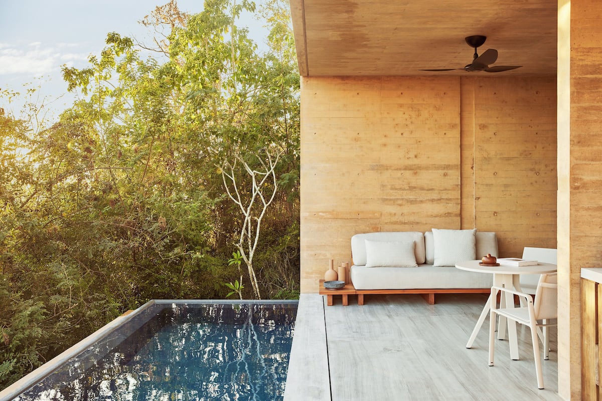 Un espace de vie extérieur moderne comprenant une piscine, une terrasse en bois et un canapé avec des coussins.
