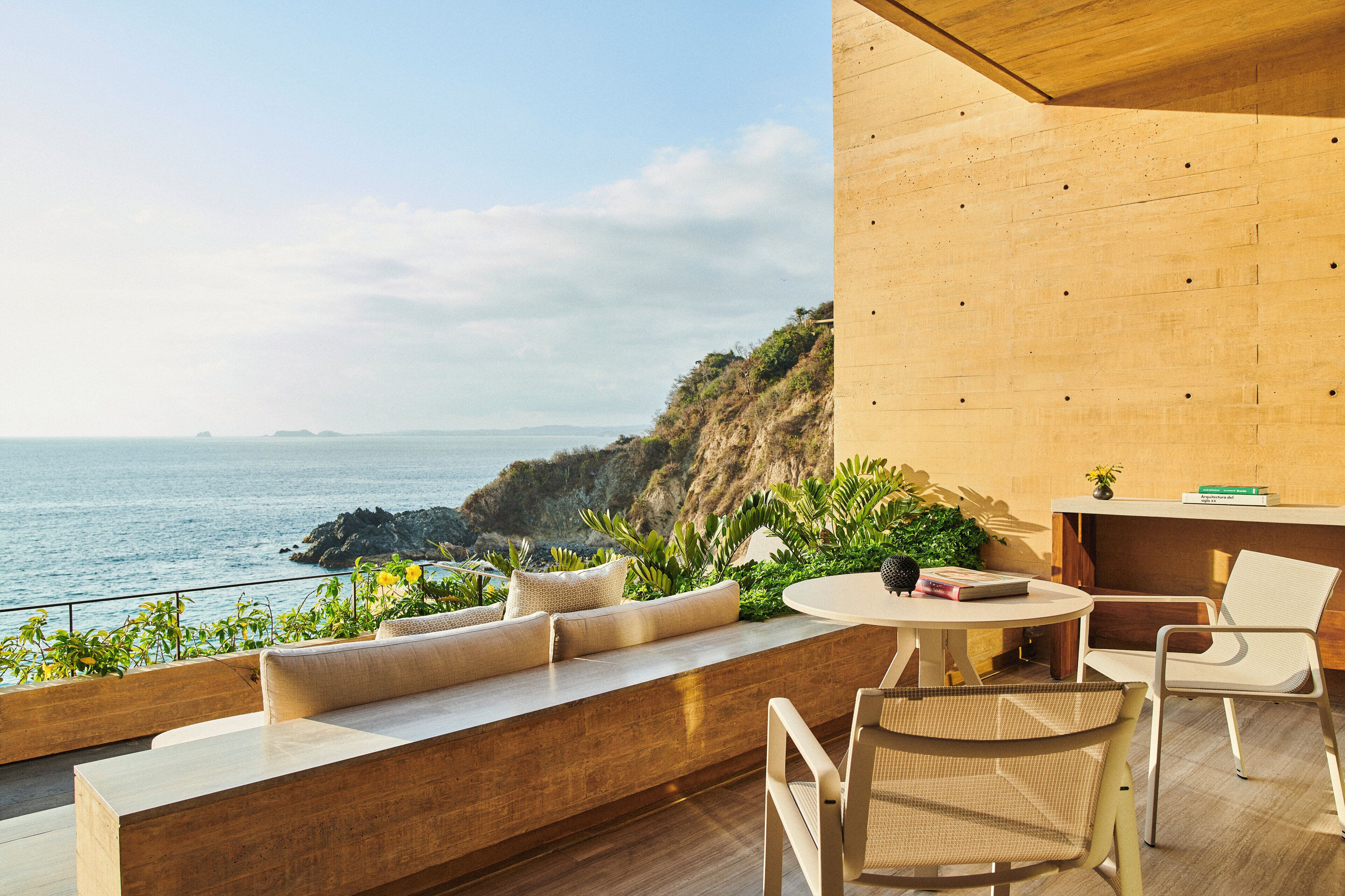 A modern outdoor seating area with a view of the ocean, wooden flooring, and a small table with chairs.