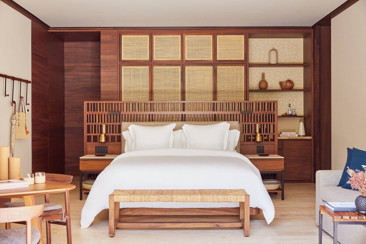 Une chambre dotée d’un grand lit, d’une tête de lit en bois, de tables de chevet, d’un petit bureau et d’un coin salon avec un banc.
