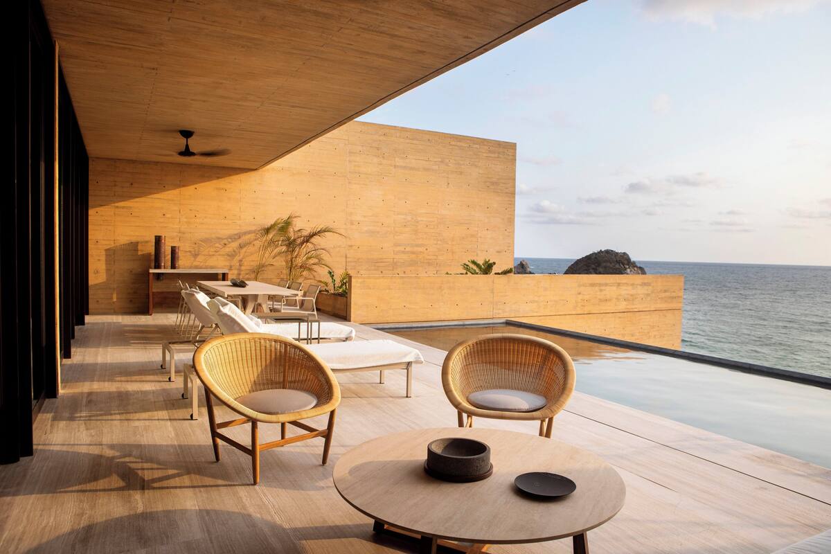 Un espace extérieur moderne, aménagé avec des fauteuils en osier et une table ronde, offrant une vue sur la mer.