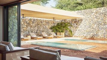 Relax by the glass-enclosed pool surrounded by lounge chairs and a natural stone wall.