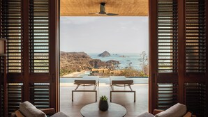 Habitación con vista al océano, dos sillones de descanso, una mesita y un ventilador de techo.