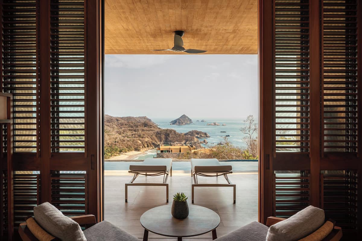 Une chambre avec vue sur l’océan, deux fauteuils confortables, une petite table et un ventilateur de plafond.