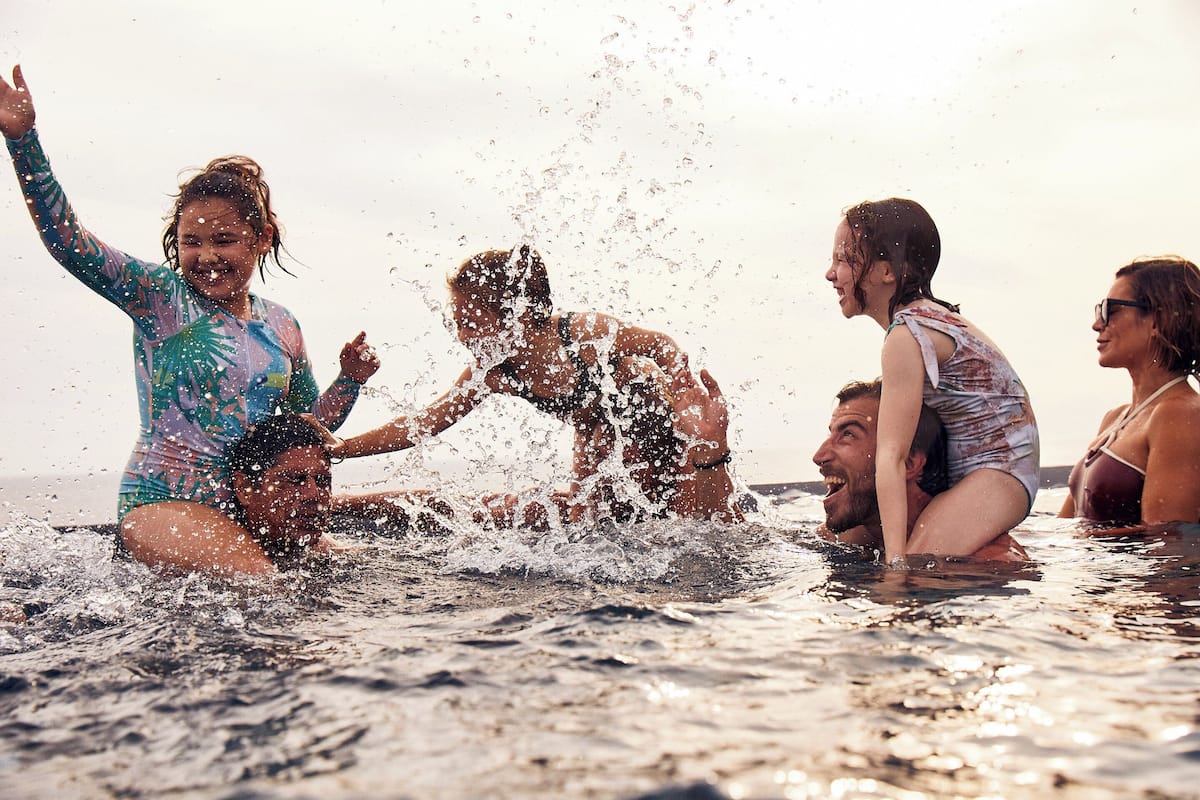 Un groupe de personnes se trouve dans une étendue d’eau, probablement une plage ou une piscine, et l’eau éclabousse autour d’eux.