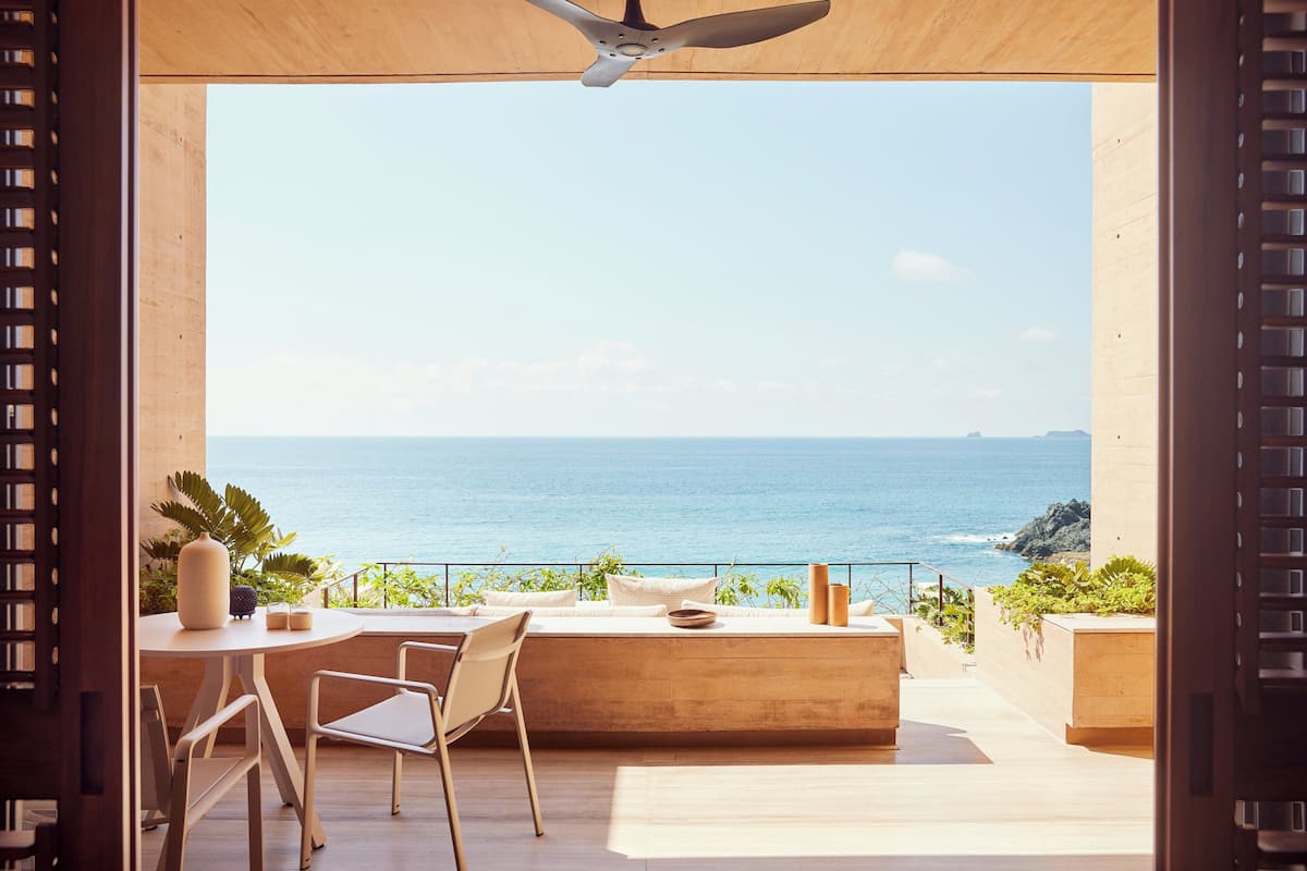 Un espace de détente extérieur moderne avec vue sur l’océan, comprenant une table, des chaises et un ventilateur de plafond.