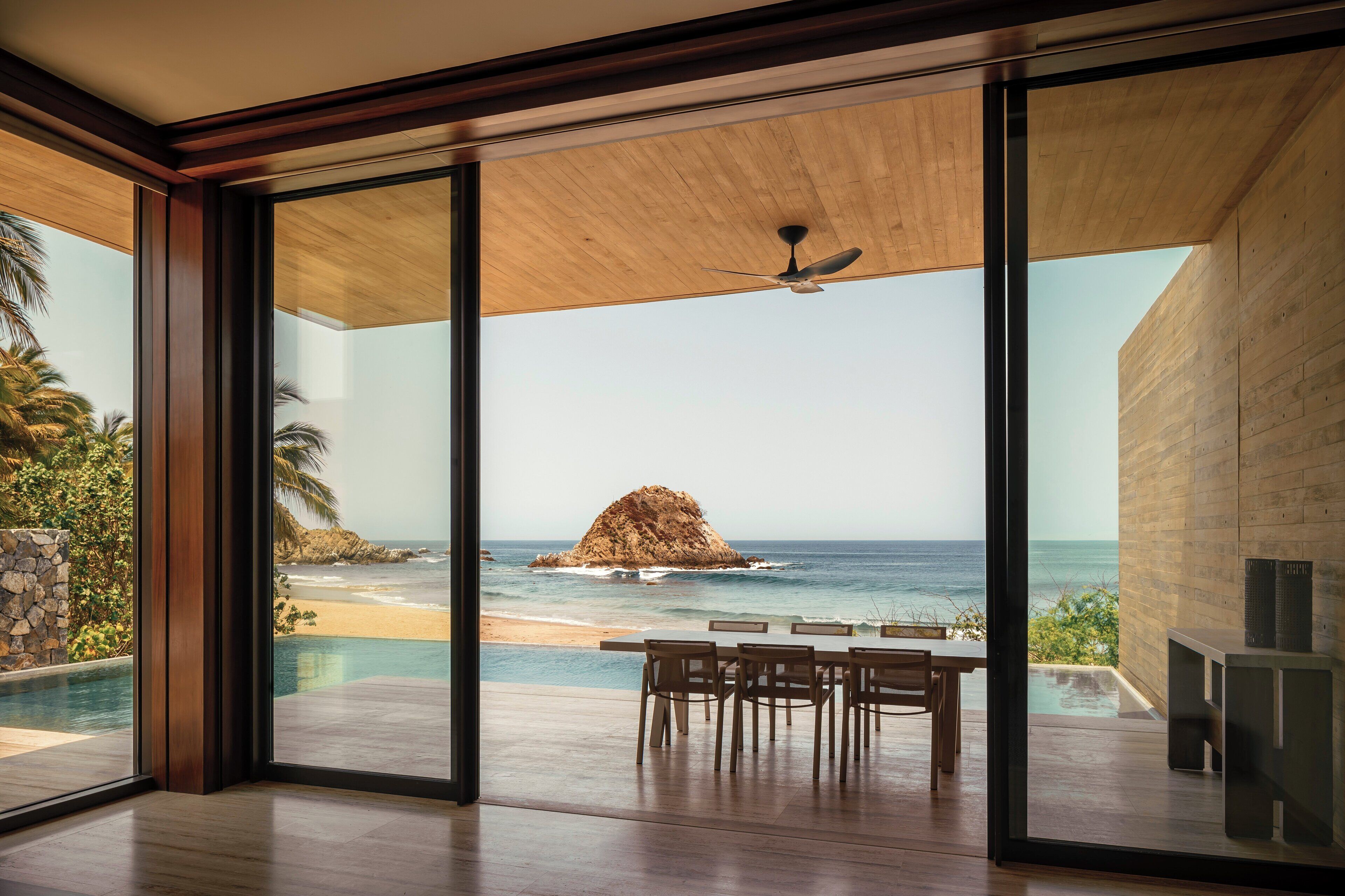 A modern interior with large glass doors leading to a balcony overlooking a beach and ocean.