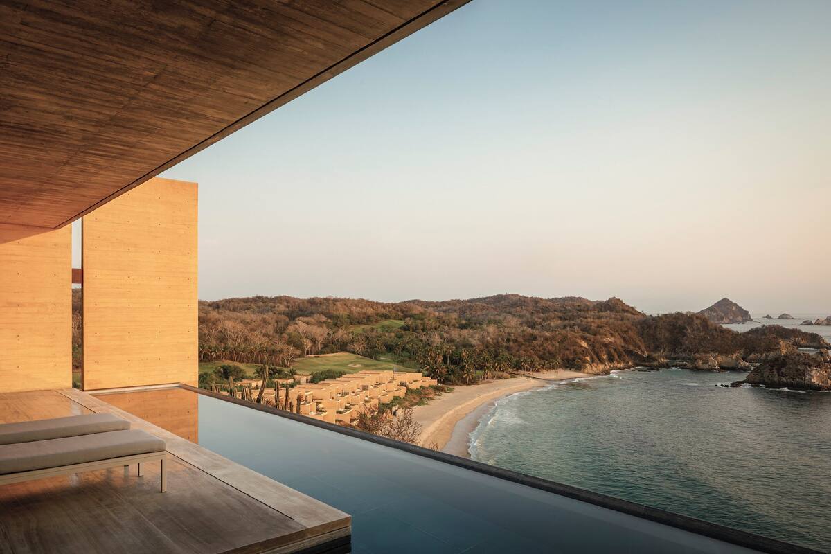 Une chambre d’hôtel moderne dotée d’un grand balcon donnant sur une plage et l’océan.