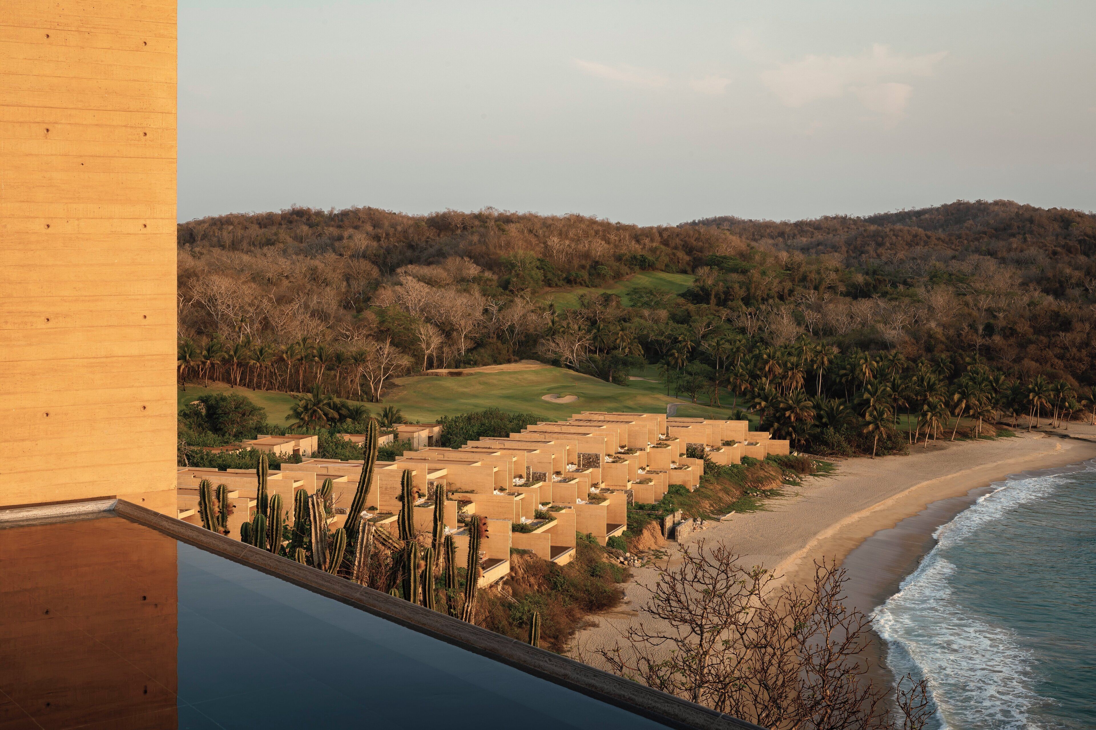 A coastal resort with multiple bungalow-style accommodations, a sandy beach, and a backdrop of dense forest.