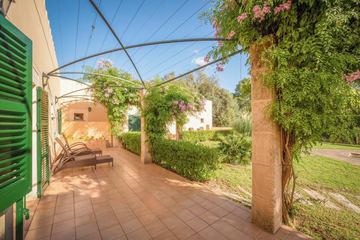 A covered outdoor area with a tiled floor, green shutters, and a bench.
