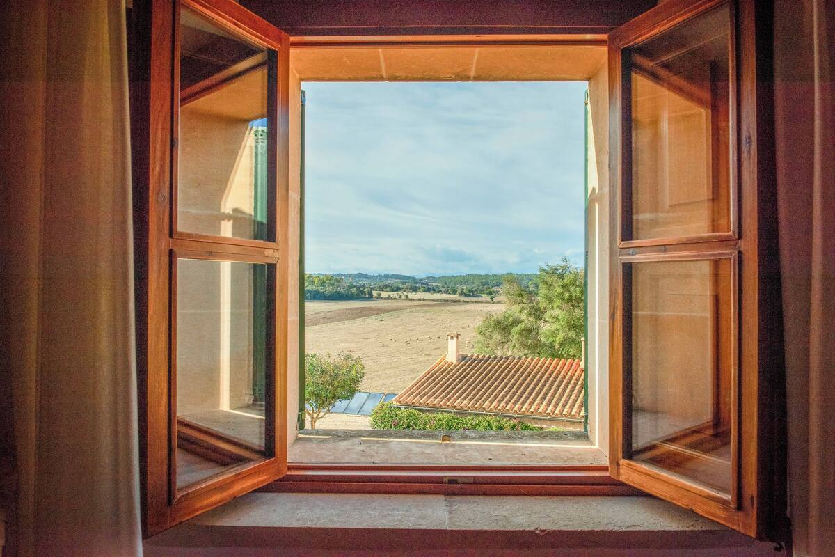 An open window with a view of a rural landscape, including fields and distant hills.