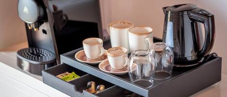 A coffee station with a coffee maker, cups, a glass carafe, and a kettle on a tray.