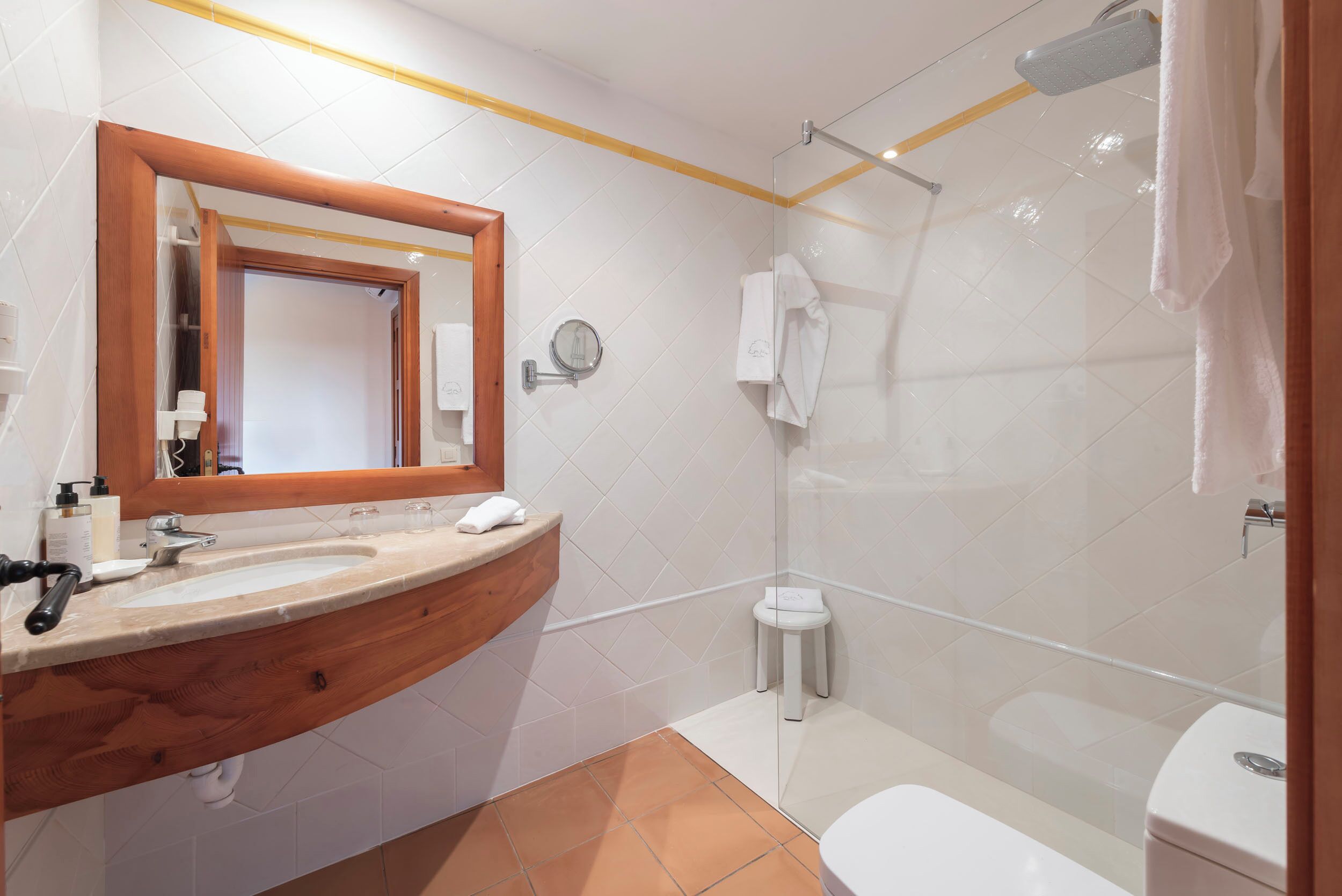 A bathroom with a wooden vanity, a mirror, a toilet, and a glass-enclosed shower.