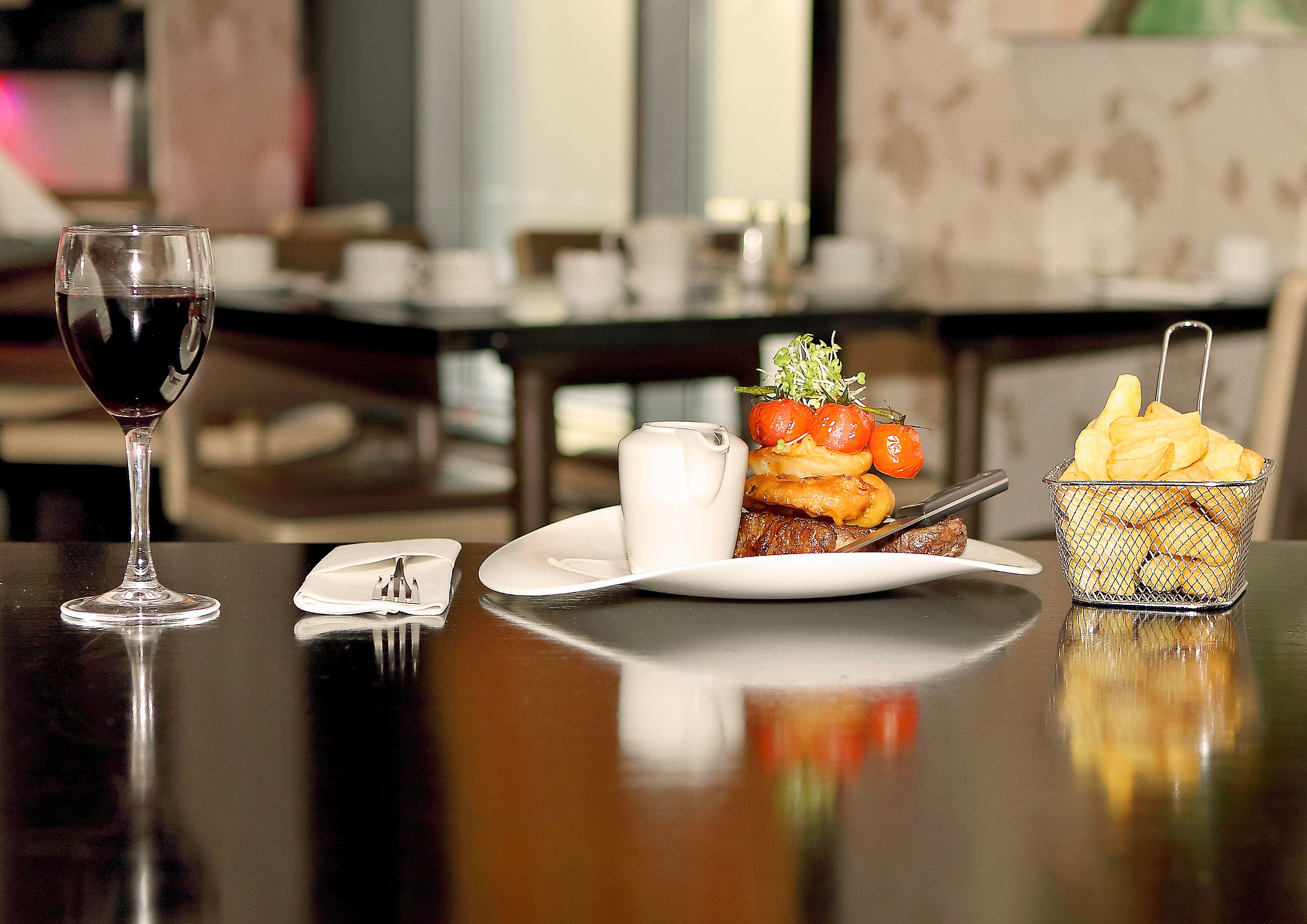 A dining table with a wine glass, a plate with food, and a basket of chips.