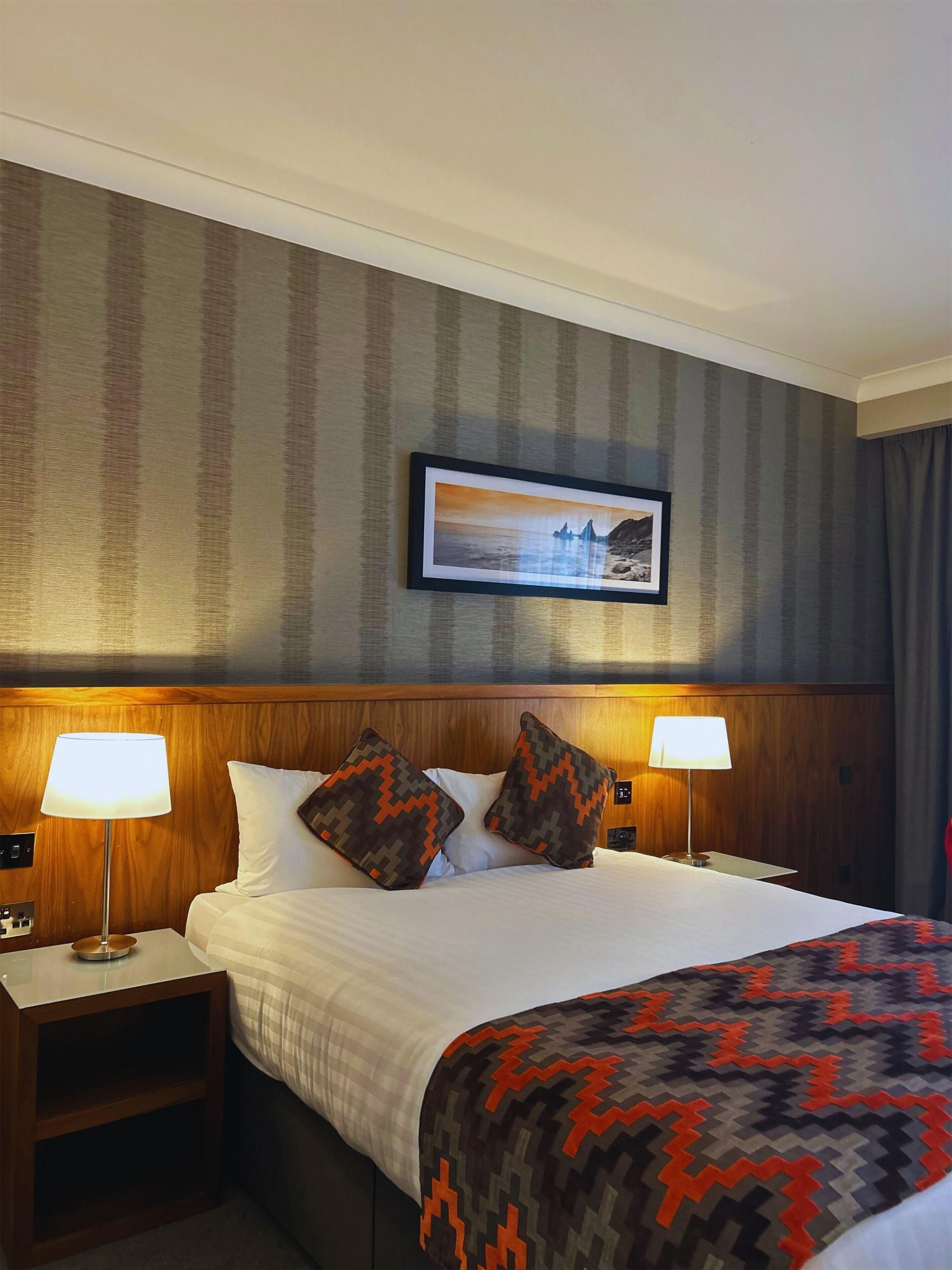 A hotel room with a large bed, two bedside lamps, a nightstand, and a framed picture on the wall.