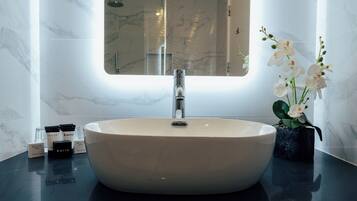Un bagno con un lavandino bianco grande, uno specchio sopra e un vaso con fiori bianchi sul ripiano.