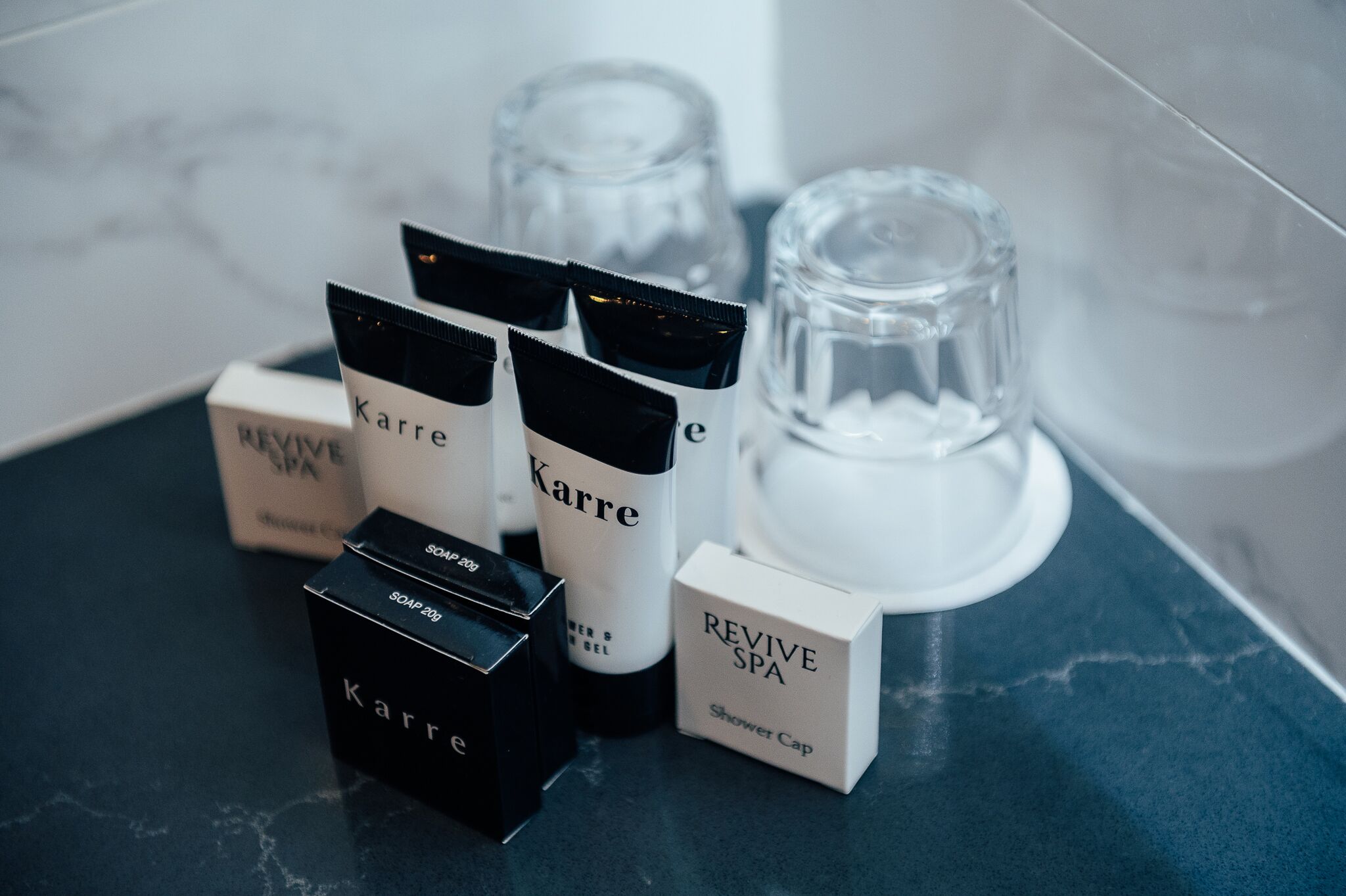 A bathroom counter with various toiletries including a shower cap, soap, and a bottle of Karre.