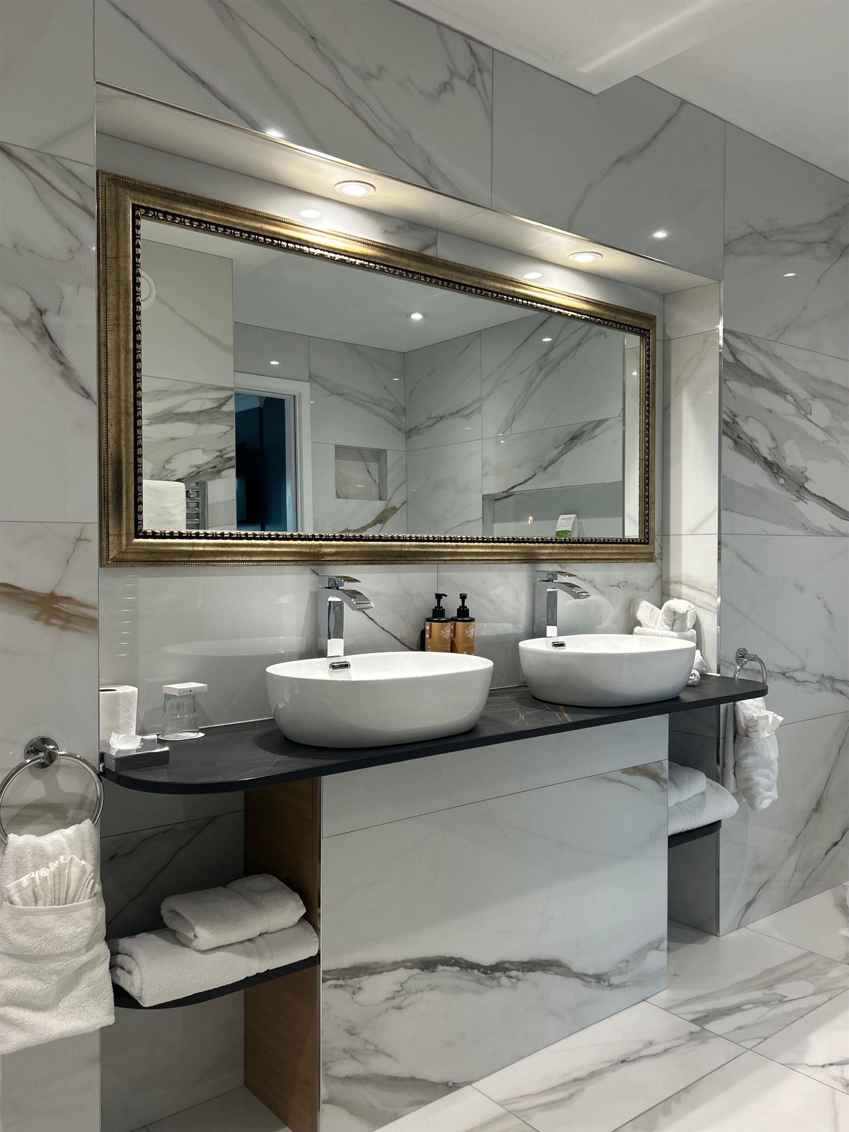 Une salle de bain moderne avec deux lavabos, un grand miroir et des murs en marbre.