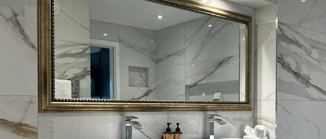 Un baño moderno con dos lavamanos, un espejo grande y paredes de mármol.