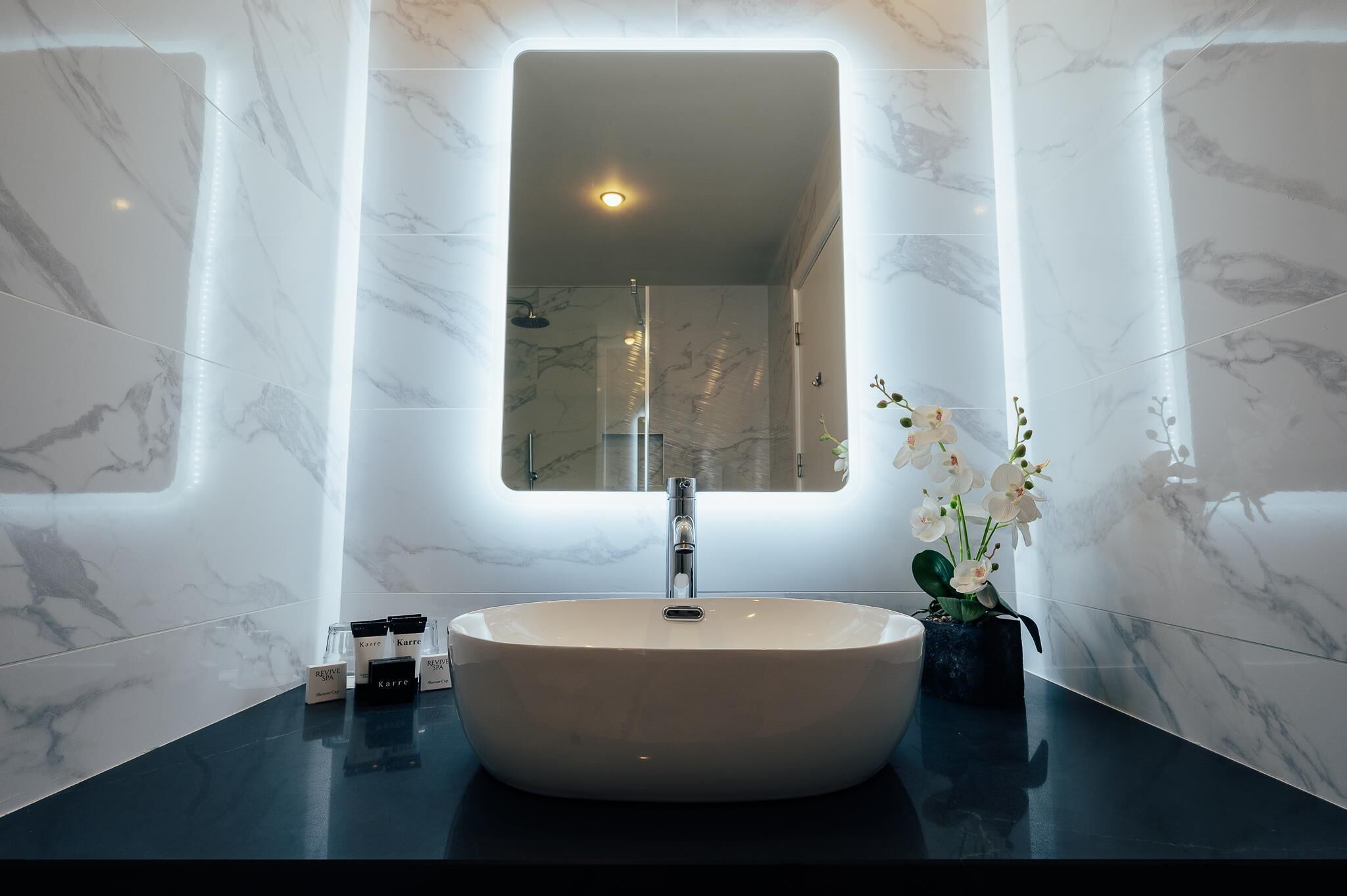Ein modernes Badezimmer mit einem großen, ovalen Waschbecken, einem rechteckigen Spiegel und Marmorwänden.