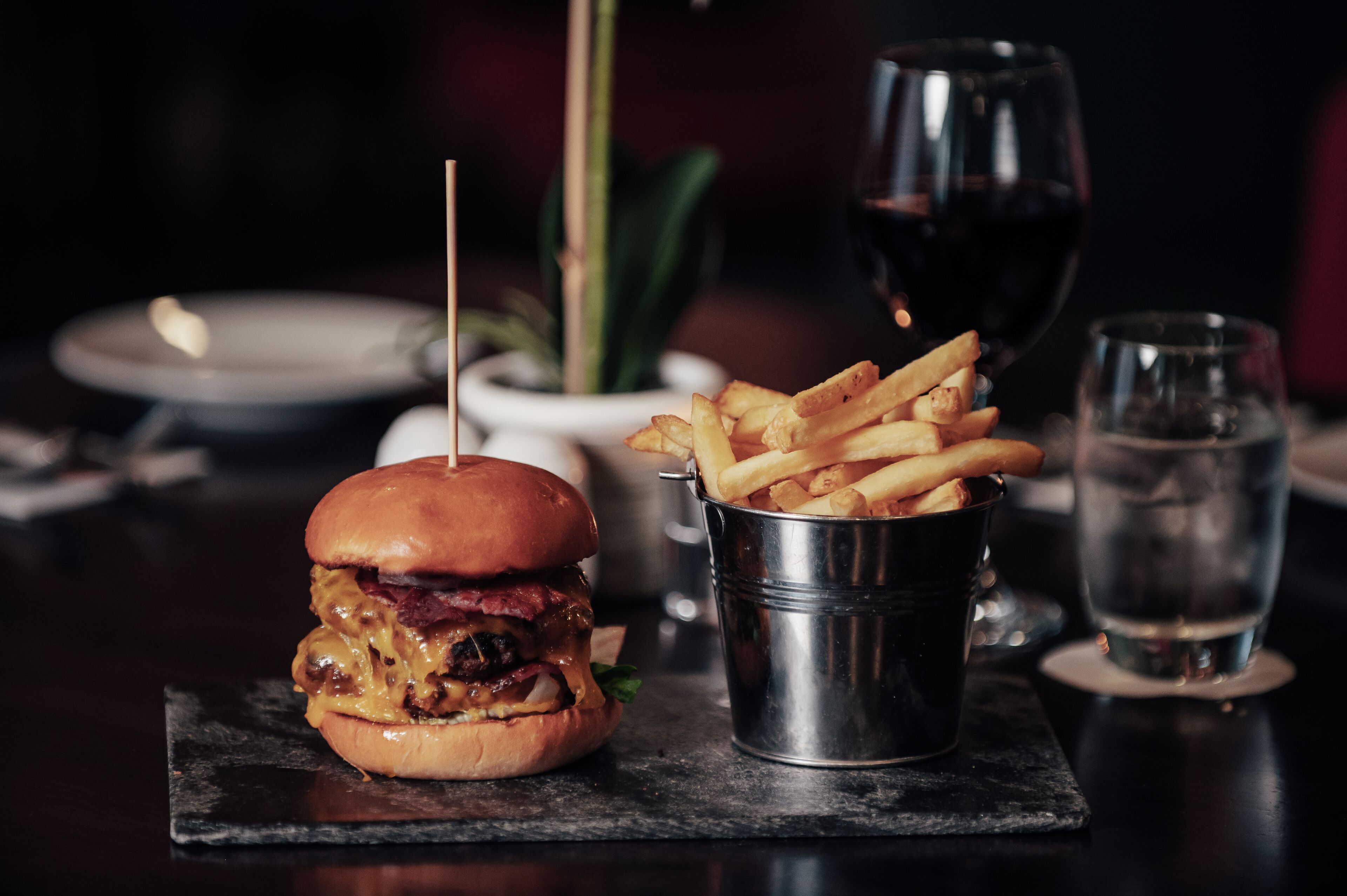 A burger with fries and a glass of red wine on a table.