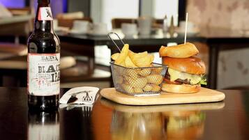 A bottle of Black IPA beer, a basket of fries, and a burger on a wooden board.