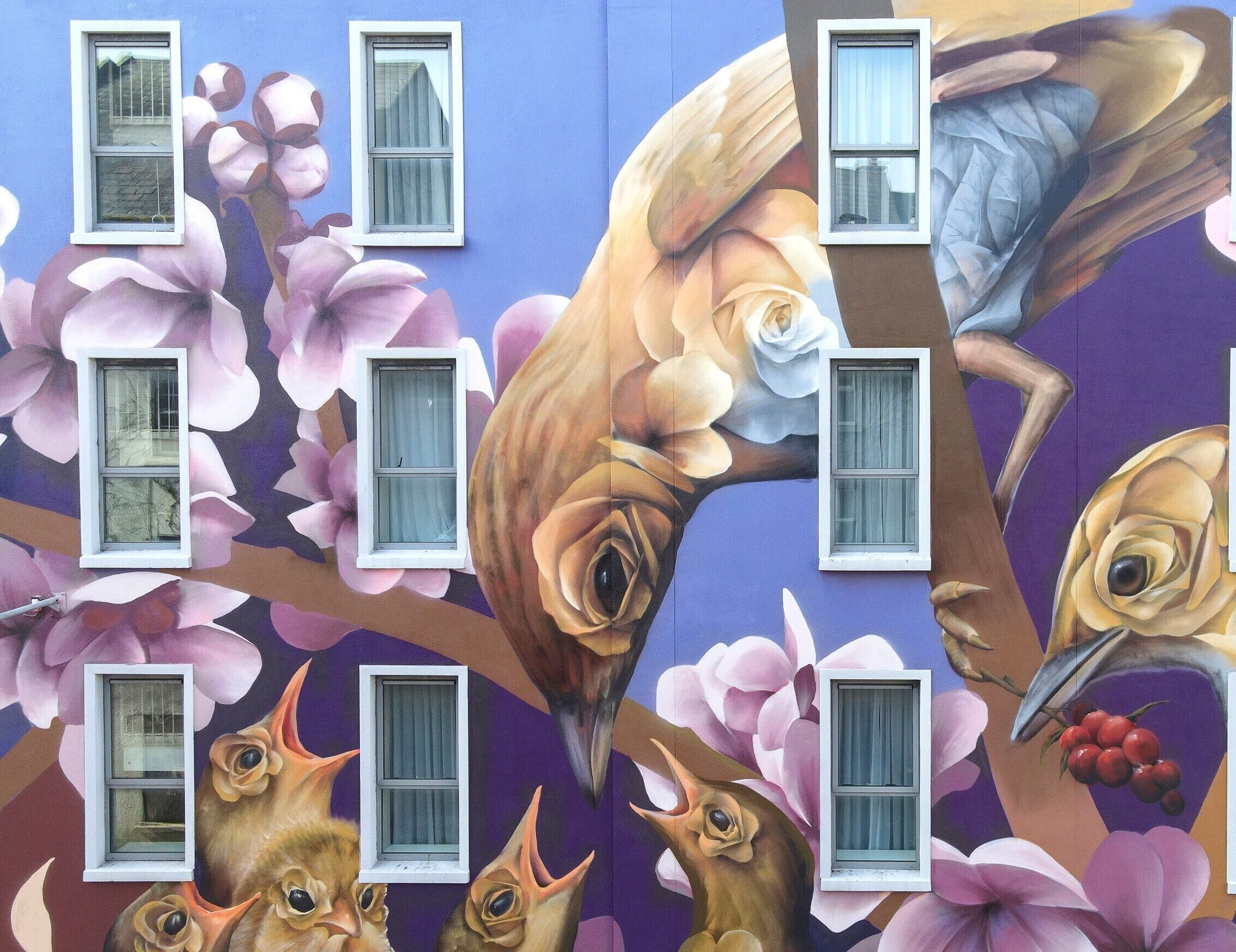 A mural with birds and flowers, windows, and a tree branch.