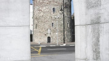 Una torre de piedra con veleta en la parte superior, una calle delante y una placa con inscripciones en un pilar.