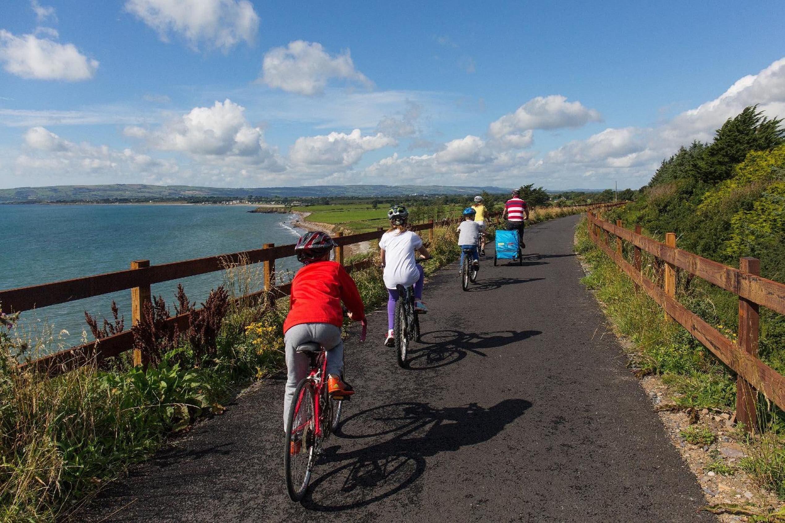 A paved path with cyclists, a wooden fence, and a view of the sea.