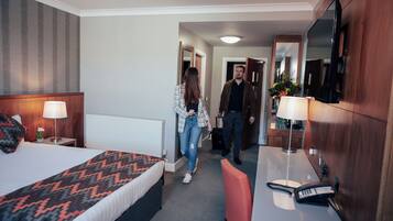 A hotel room with a bed, bedside table, lamp, and a desk with a telephone.