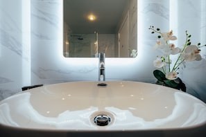 Bathroom features a large oval sink under a rectangular mirror, flanked by marble walls and a decorative orchid arrangement.