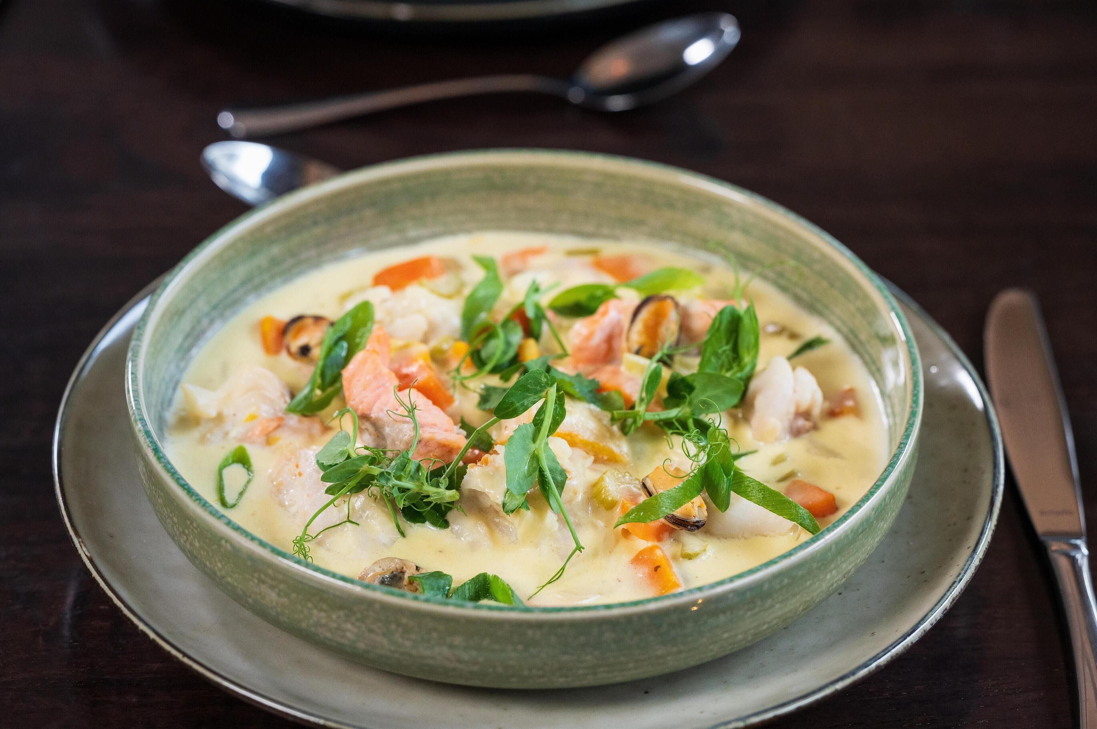 A bowl of creamy seafood soup garnished with herbs, served on a ceramic plate.