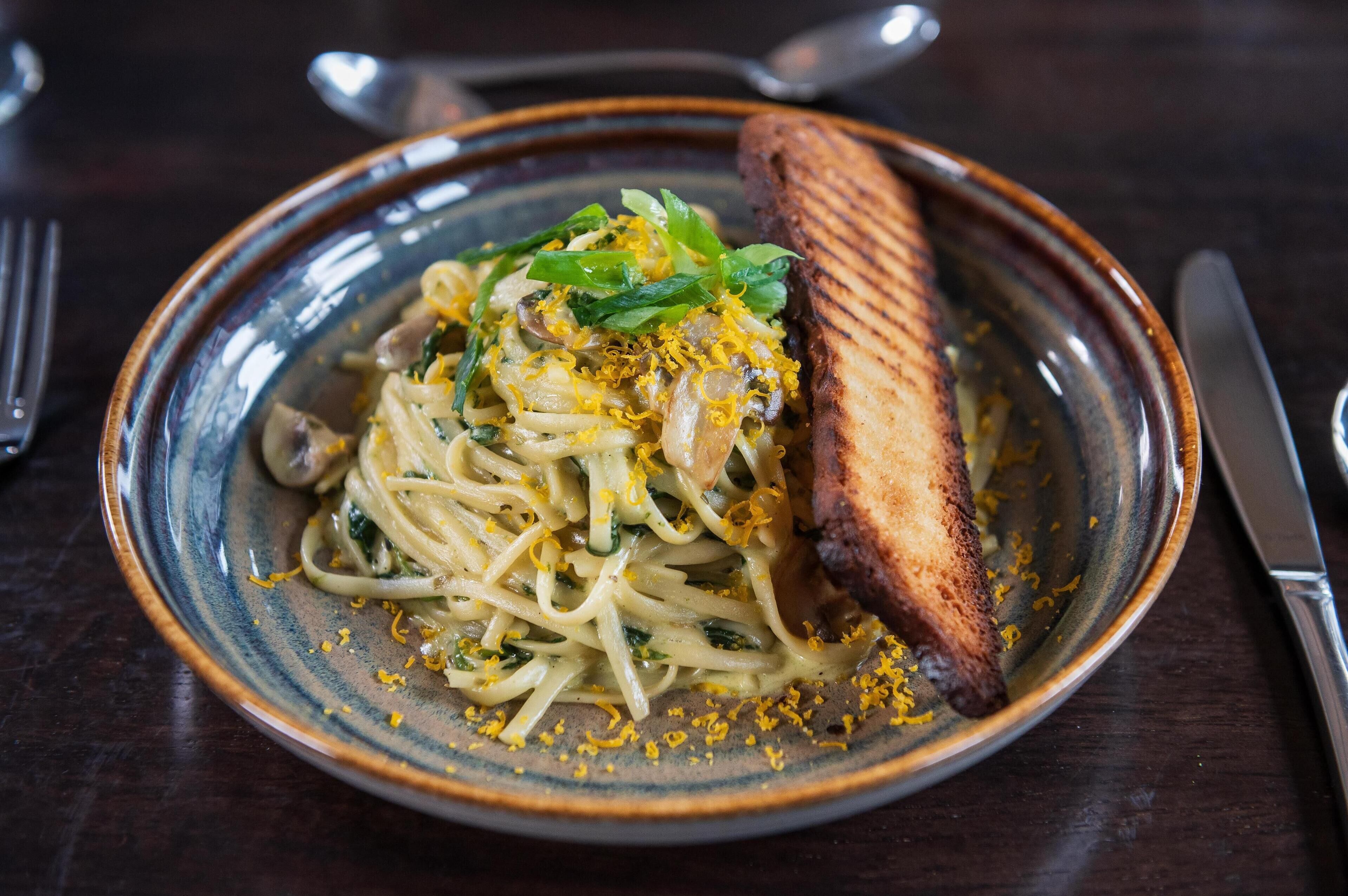 A plate of pasta with lemon zest and a grilled item, possibly a piece of meat, on a ceramic plate.