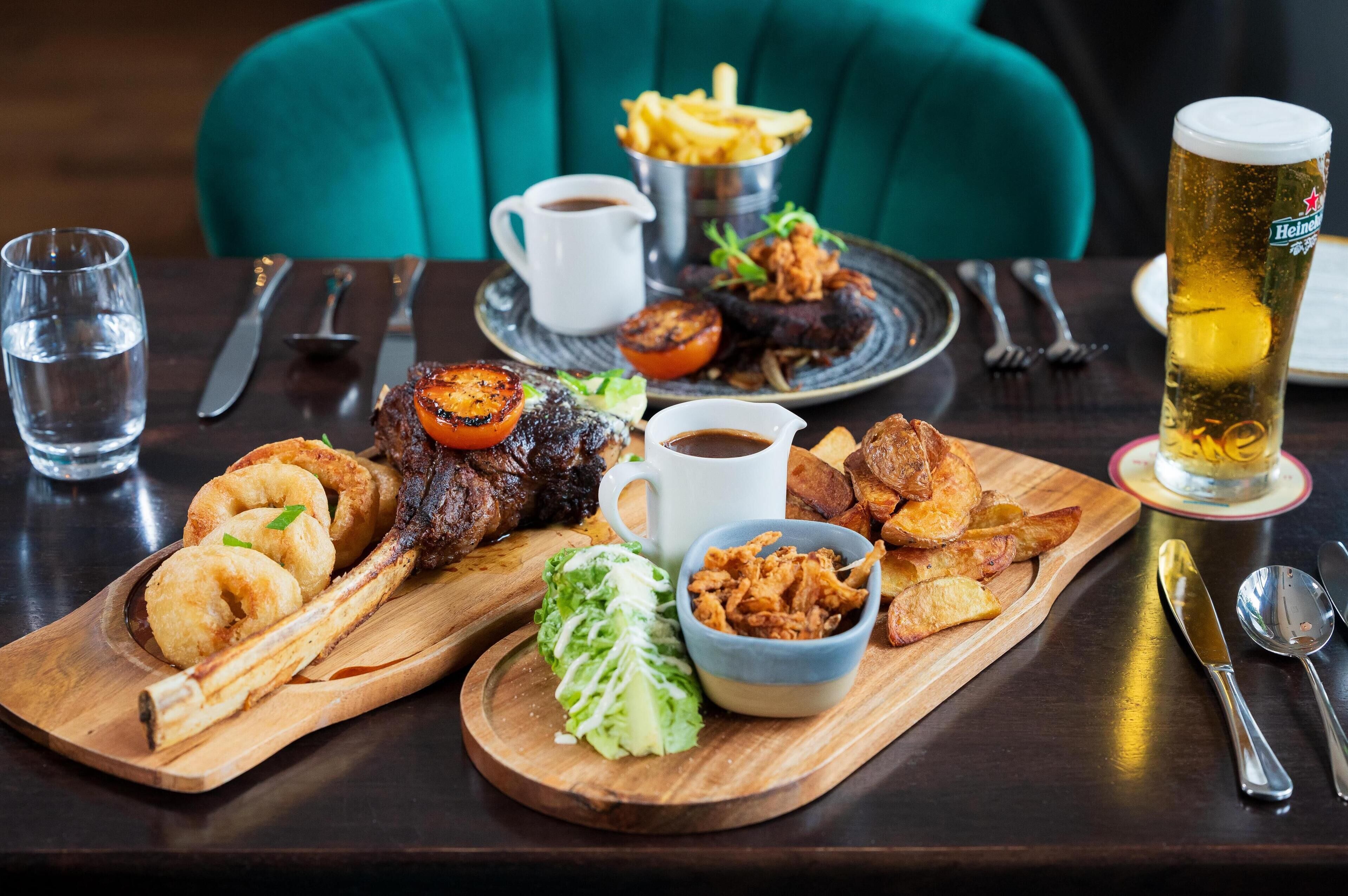 A dining table with various dishes, including steak, fries, and a beer glass.