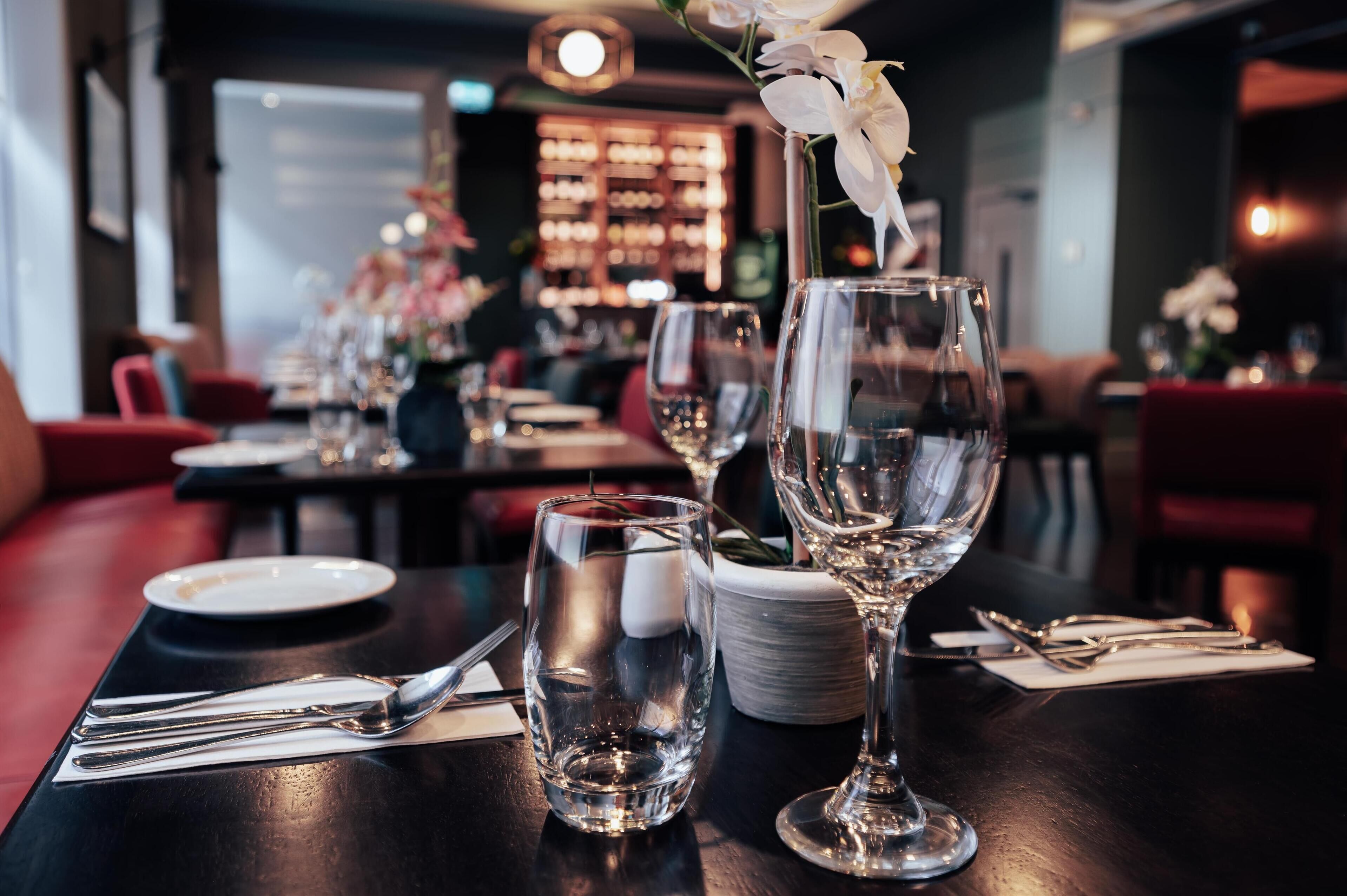 Una mesa de restaurante dispuesta con copas de vino, platos y cubiertos.
