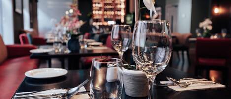 Una mesa de restaurante dispuesta con copas de vino, platos y cubiertos.