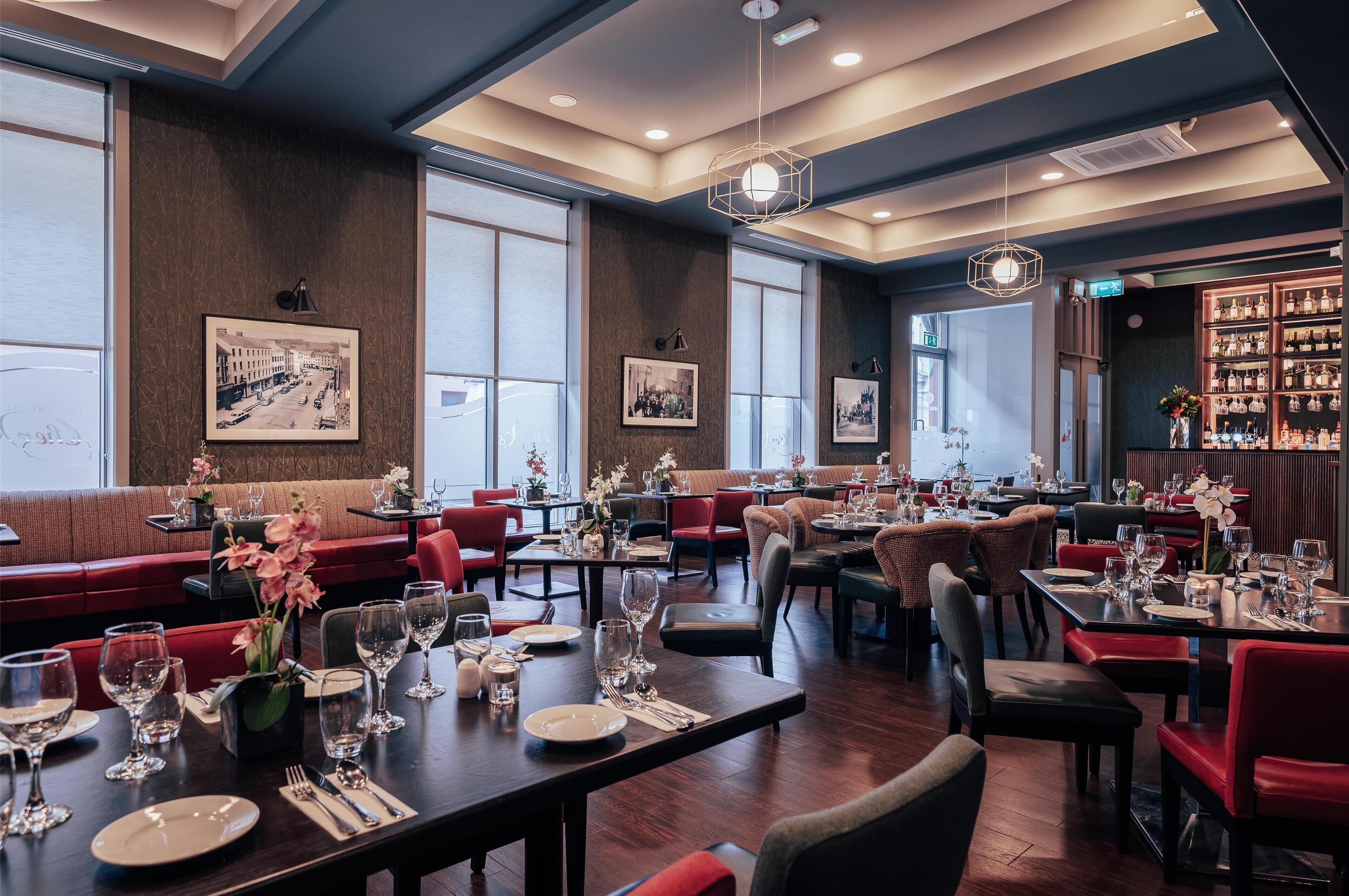 A restaurant with multiple dining tables set for guests, red upholstered seating, and framed pictures on the walls.