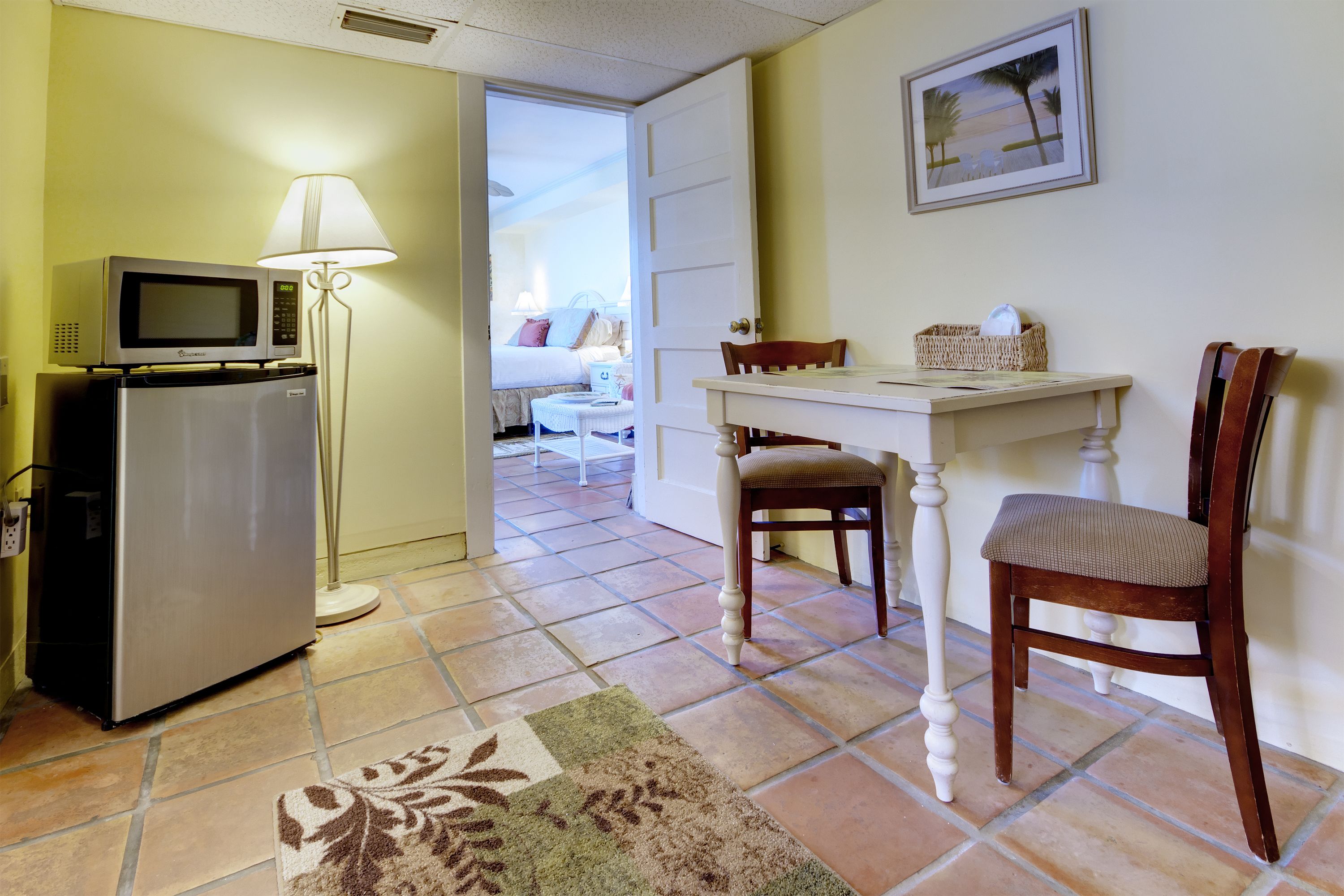 A hotel room with a kitchenette, a dining area, and a view into the bedroom.