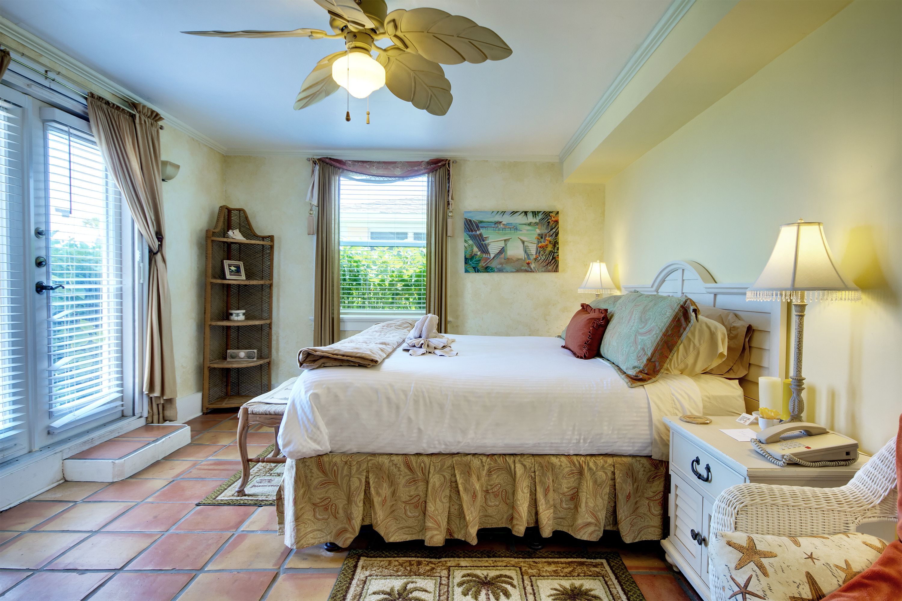 A bedroom with a bed, a nightstand, a chair, a ceiling fan, and a window with curtains.