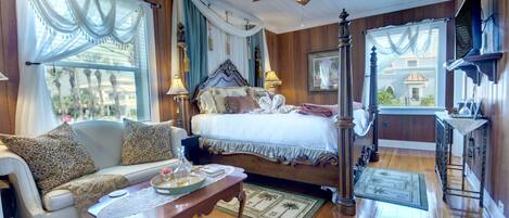 A cozy room with a bed, a sofa, a wooden floor, a ceiling fan, and a window with curtains.