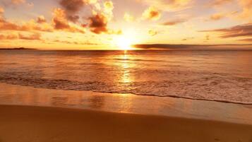 A beach at sunset with a calm sea and a clear sky.
