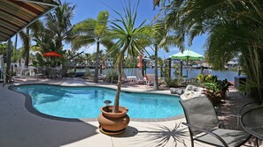 A pool area with lounge chairs, a palm tree, and a view of the water.