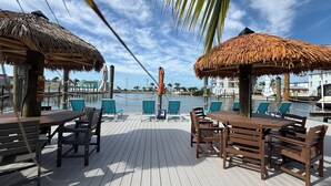 A wooden deck with thatched umbrellas, lounge chairs, and a view of the water. - Manatee Bay Inn - Near Fishing Pier Fort Myers Beach (Fort Myers Beach)