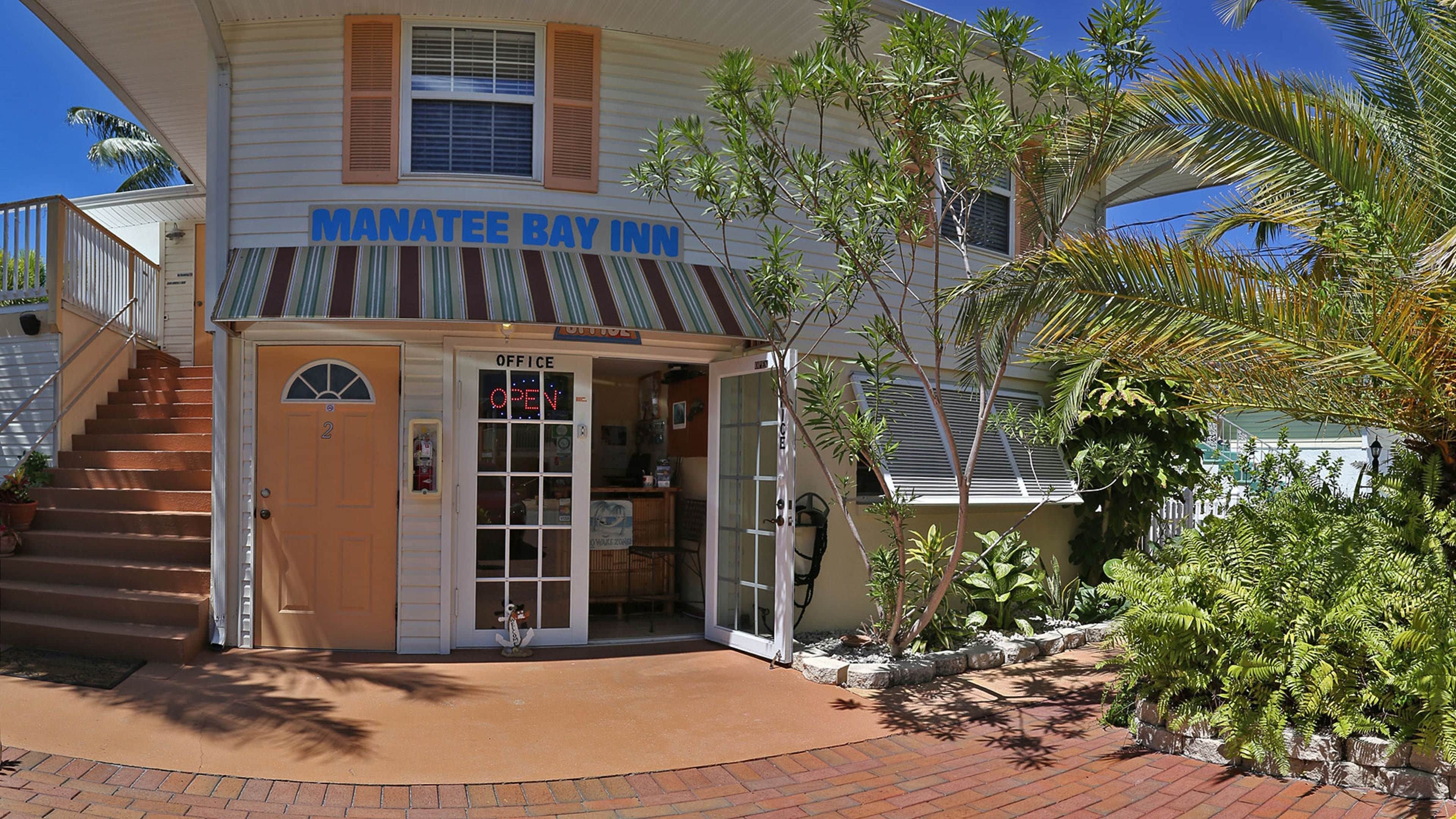 A two-story building with a sign reading "Manatee Bay Inn." There is a staircase leading to the entrance, and the building has a covered porch area.