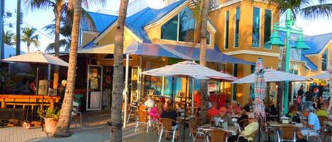 An outdoor dining area with tables and chairs, palm trees, and a building with a blue roof.
