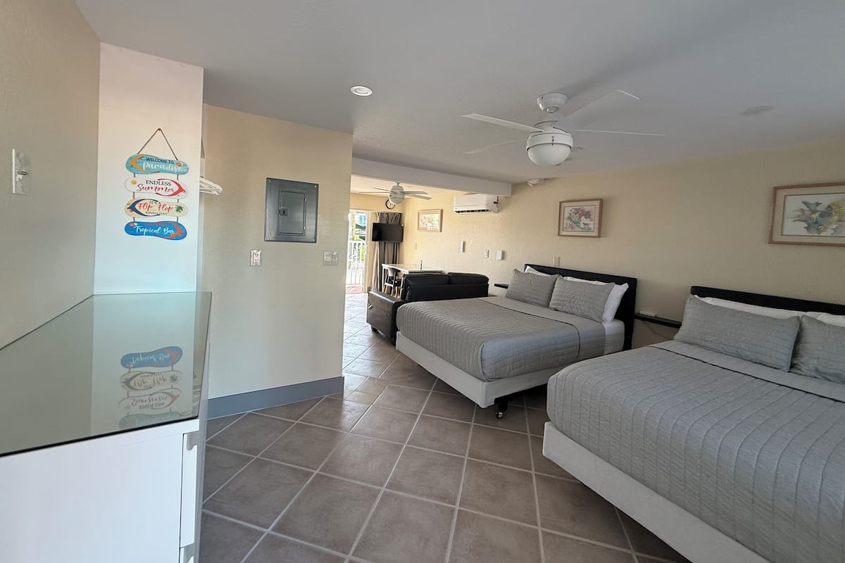 A hotel room with two beds, a ceiling fan, a TV, and a balcony with a view.