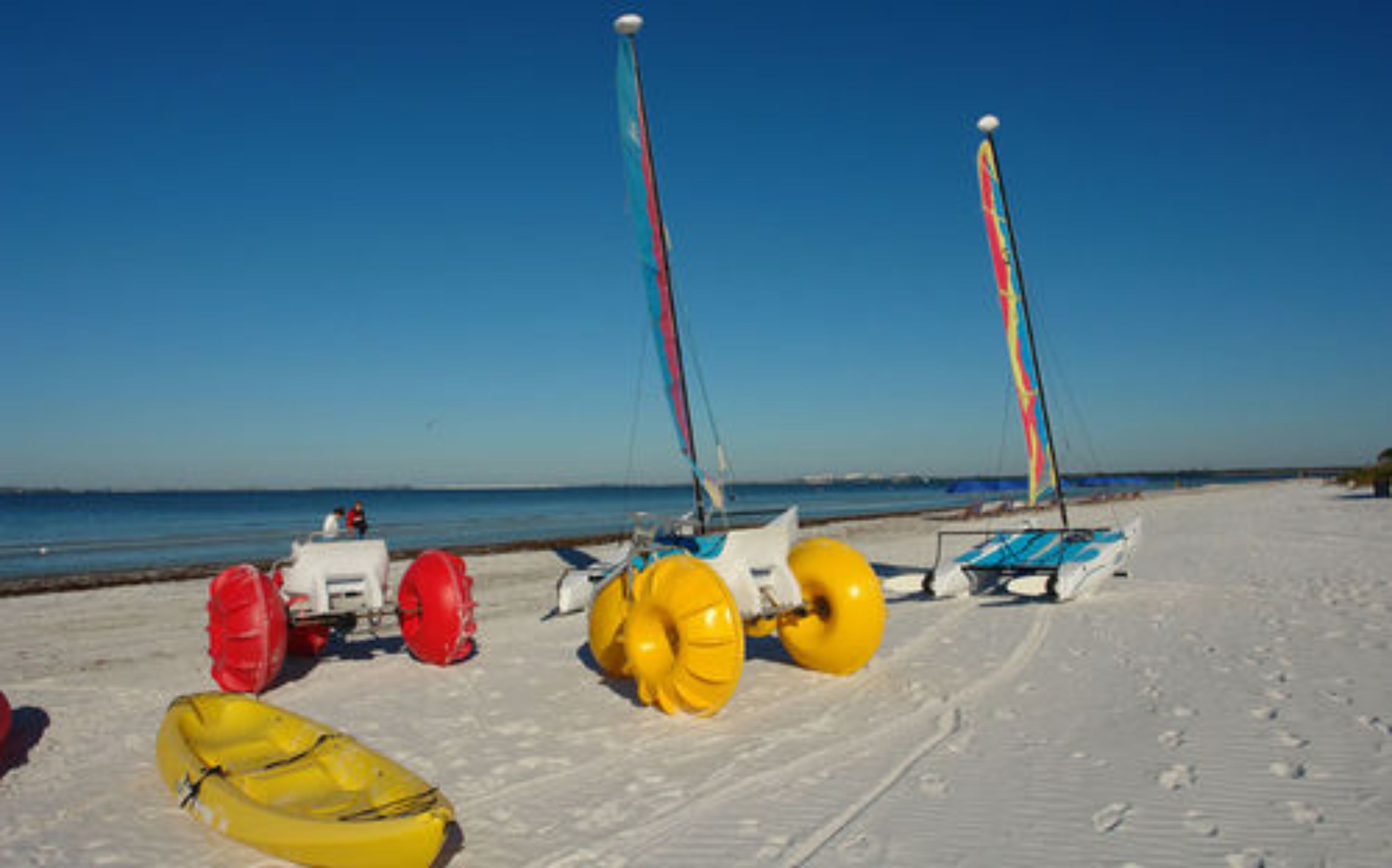 A beach with a sailboat and a yellow inflatable raft.