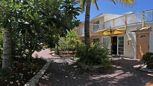 A hotel with a paved walkway, outdoor seating, and a yellow umbrella. - Manatee Bay Inn - Near Fishing Pier Fort Myers Beach (Fort Myers Beach)