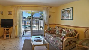 A living room with a sofa, a coffee table, a television, and a view of a pool and outdoor area.