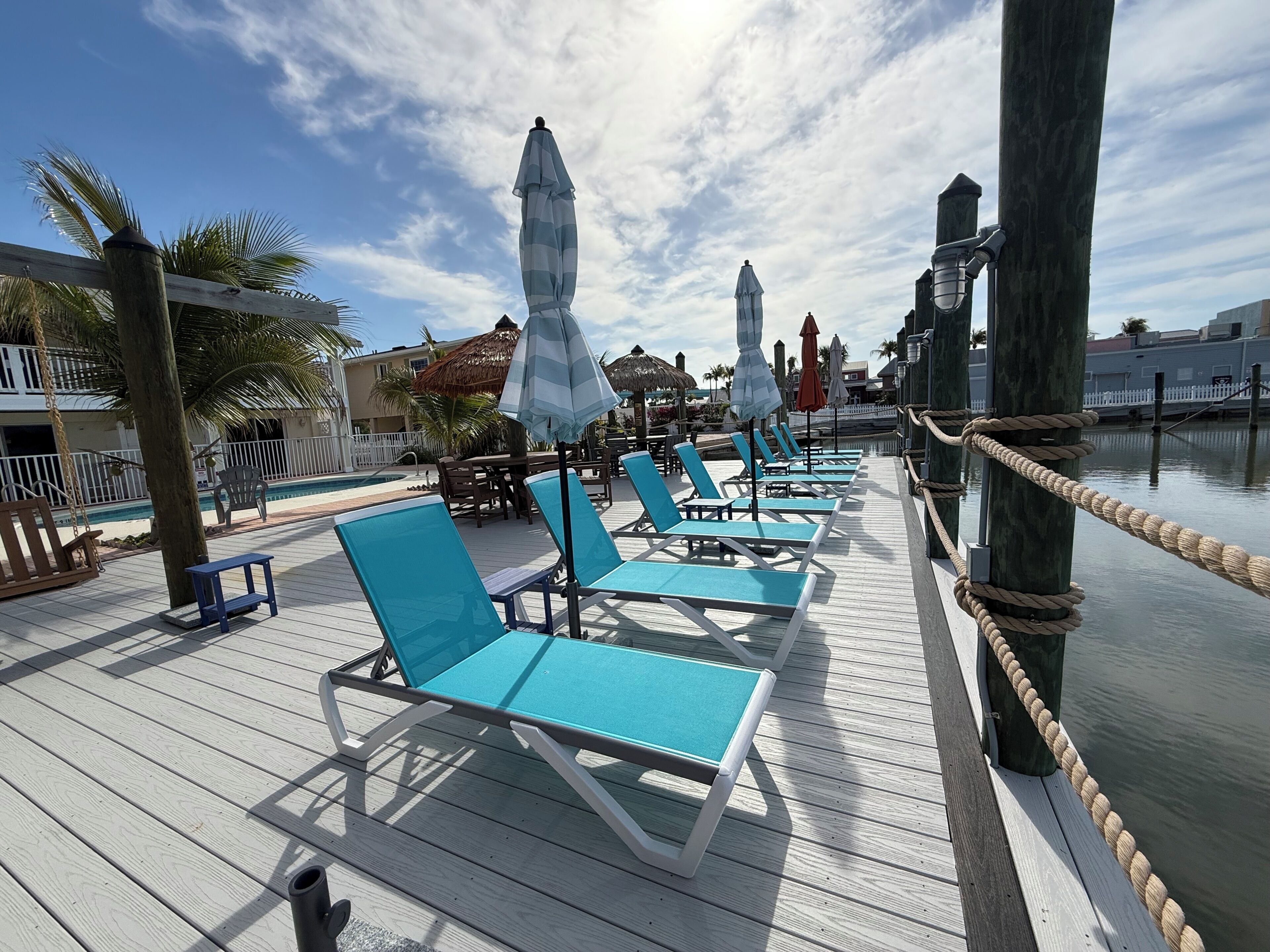 A deck with lounge chairs and umbrellas, a pool, and a wooden railing.